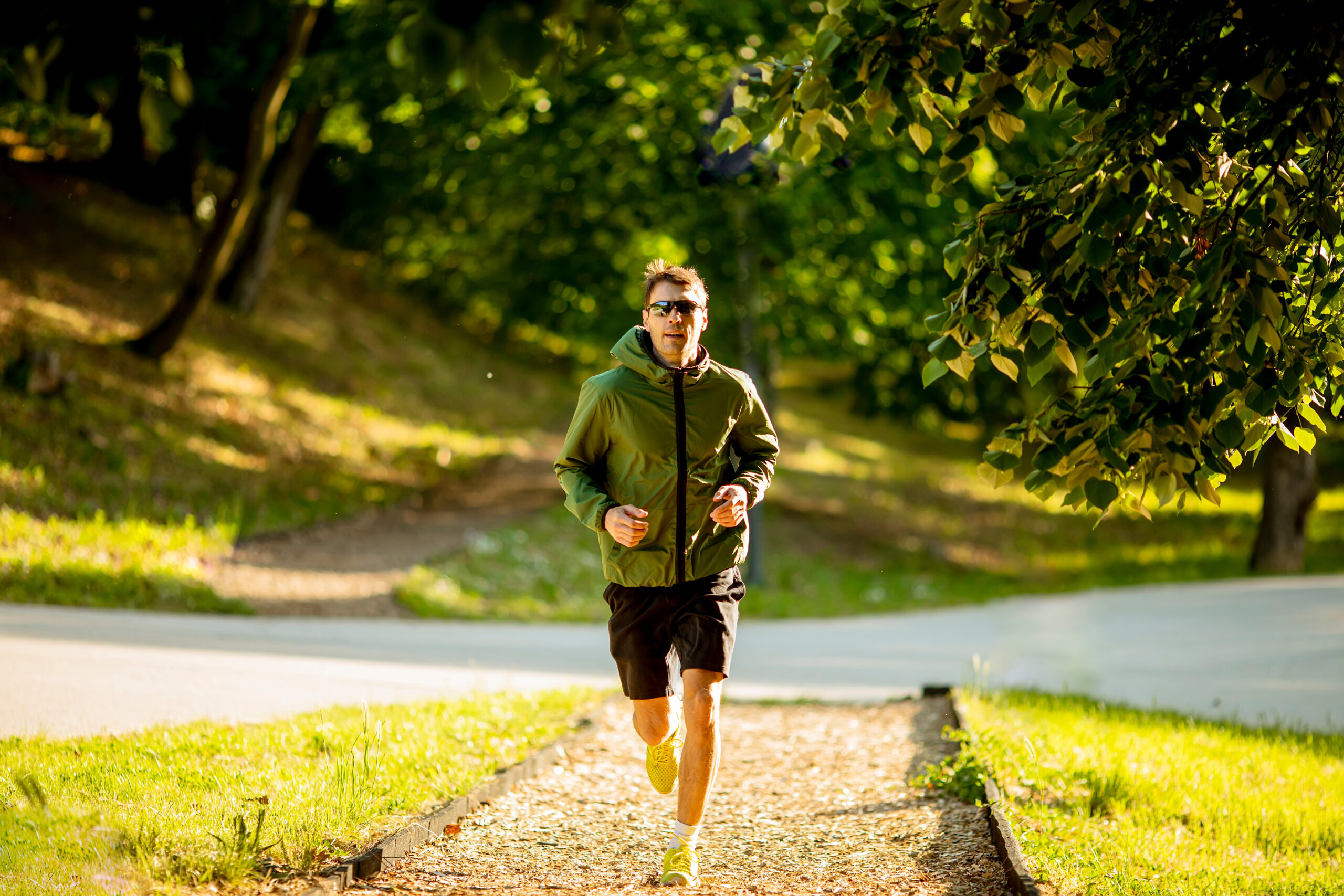 Athletic young man running while doing workout in sunny green park